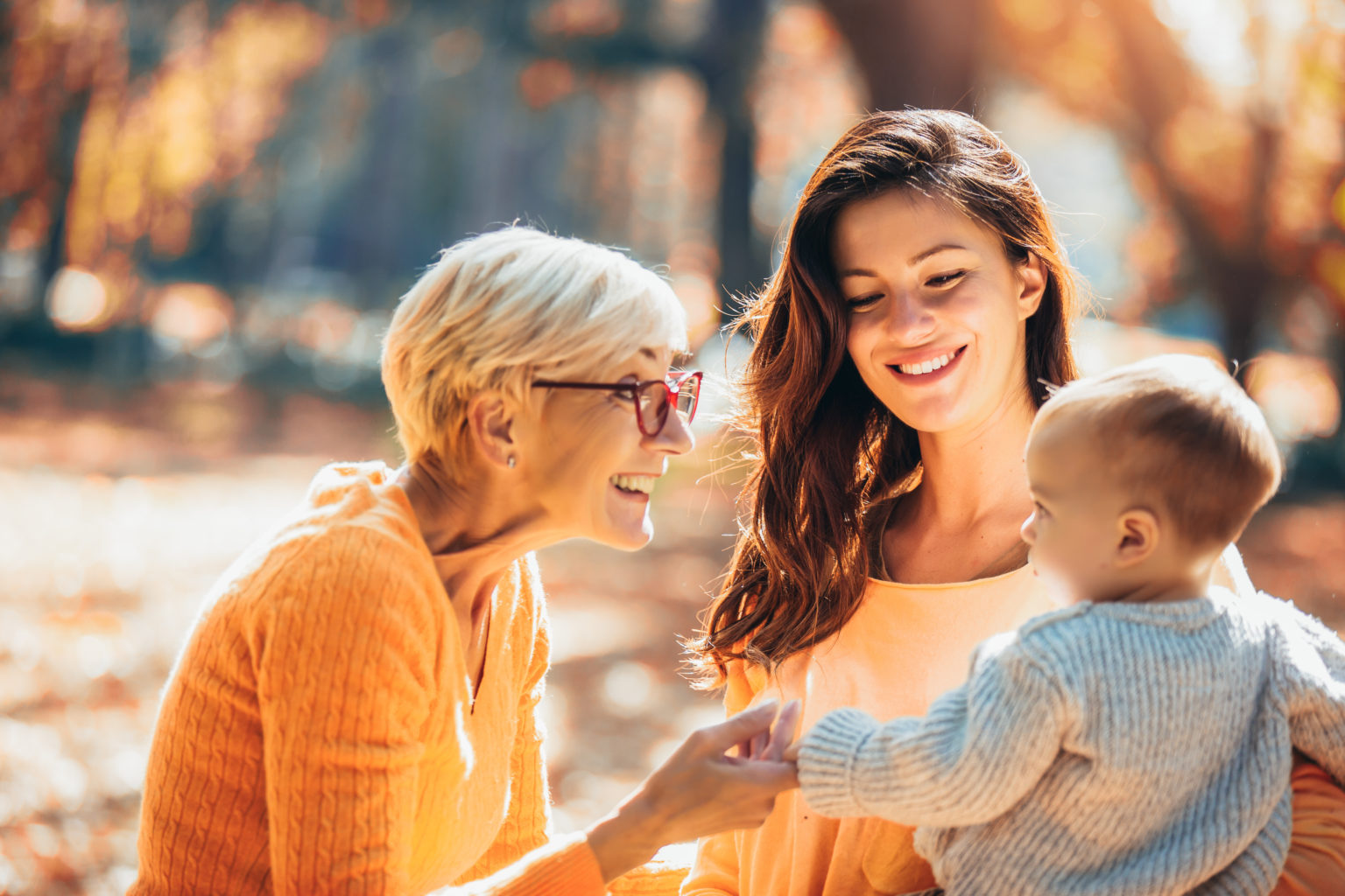 Grandmother and mother smiling at baby in autumn park after visiting dentist in Richmond Hill.